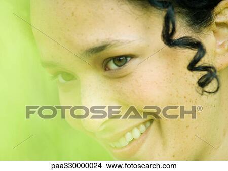 Picture - Young woman's smiling face, green blur in foreground. Fotosearch
