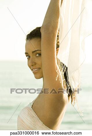 Stock Photograph - Woman holding up scarf behind head, ocean in background. Fotosearch