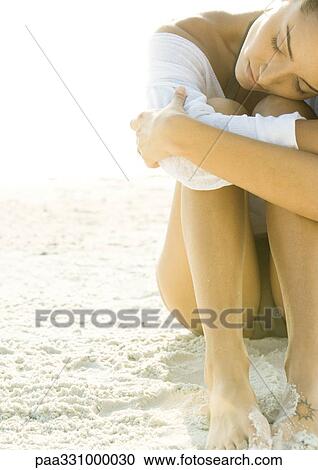 Stock Image - Woman sitting on sand, resting head on knees. Fotosearch
