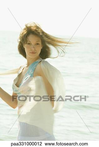 Stock Image - Woman standing in front of ocean in wind. Fotosearch