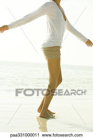 Stock Image - Woman standing on beach with arms out, neck down. Fotosearch