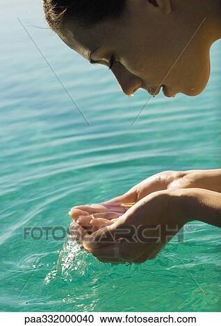 Stock Image - Woman leaning face over water, cupping water in hands. Fotosearch