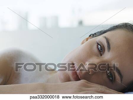 Stock Photo - Woman resting head against edge of bathtub, eyes half closed, close-up. Fotosearch