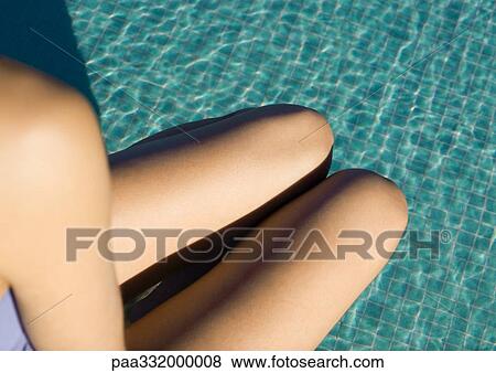 Stock Photo - Woman's shoulder and legs seen over pool water, high angle view. Fotosearch