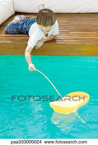 Boy lying on floor near edge of pool, playing with toy boat View Large Photo Image Picture - Boy lying on floor near edge of pool, playing with toy boat. Fotosearch