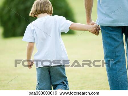 Boy walking next to father, holding his hand, rear view View Large Photo Image Stock Photo - Boy walking next to father, holding his hand, rear view. Fotosearch