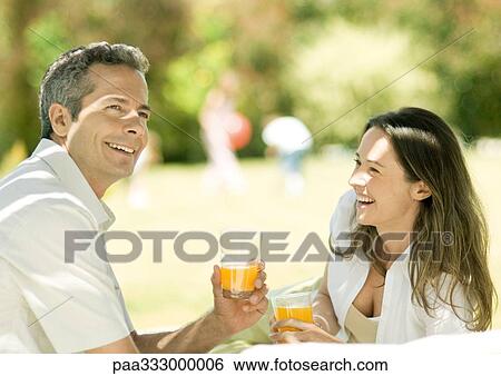 Stock Photograph - Couple holding glasses of juice outdoors. Fotosearch
