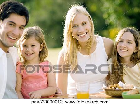 Family sitting at table outdoors, smiling View Large Photo Image Stock Image - Family sitting at table outdoors, smiling. Fotosearch