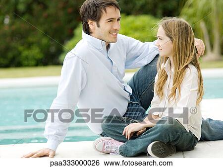 Stock Photograph - Father and daughter sitting by edge of pool. Fotosearch