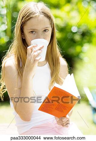 Girl drinking and holding book outdoors View Large Photo Image Picture - Girl drinking and holding book outdoors. Fotosearch