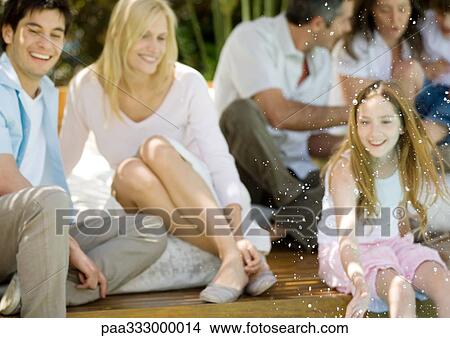 Girl splashing water, family relaxing in background View Large Photo Image Picture - Girl splashing water, family relaxing in background. Fotosearch