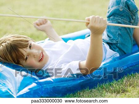 Stock Image - Little boy lying on inflatable raft, on grass. Fotosearch