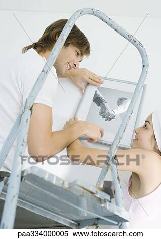 Stock Photography - Couple hanging up photo on wall. Fotosearch