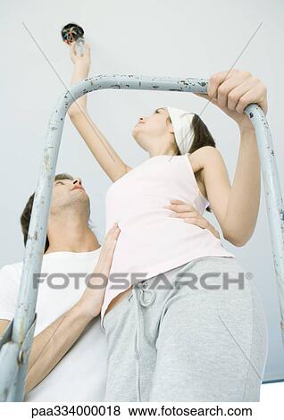 Stock Photo - Man holding man on ladder as she changes lightbulb. Fotosearch
