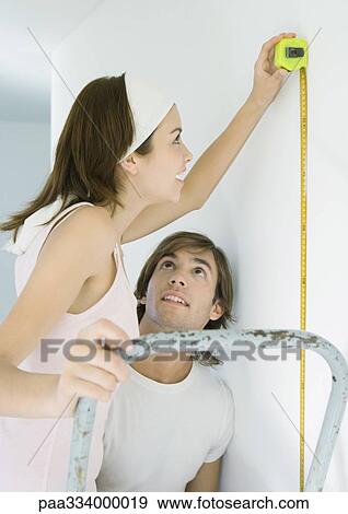 Woman on ladder using measuring tape as man watches View Large Photo Image Stock Photo - Woman on ladder using measuring tape as man watches. Fotosearch
