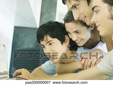 Stock Photo - Four young adult friends looking at computer screen together. Fotosearch