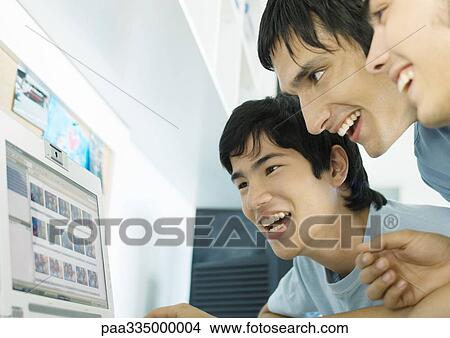Picture - Three young friends looking at computer screen. Fotosearch