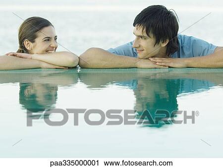 Stock Image - Young couple smiling at each other by water. Fotosearch