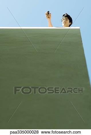 Young man holding out cell phone, low angle view View Large Photo Image Stock Photo - Young man holding out cell phone, low angle view. Fotosearch