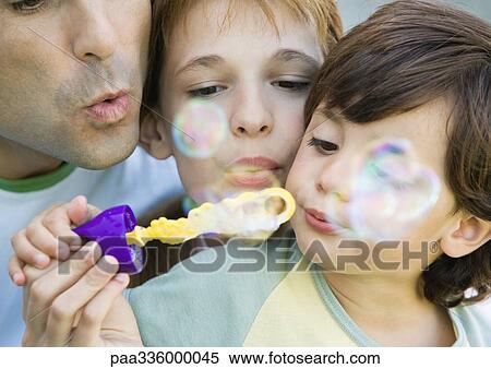 Stock Photography - Father having fun with his two chiildren, blowing soap bubbles together, portrait, extreme close-up. Fotosearch
