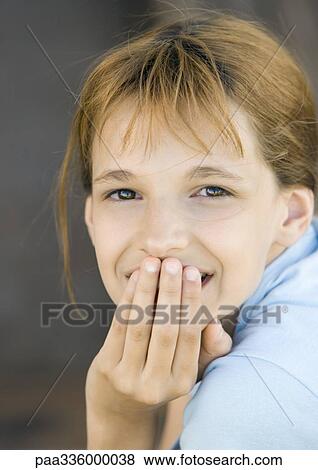 Stock Photo - Girl covering mouth looking at camera, smiling, portrait, close-up. Fotosearch