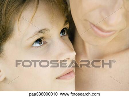 Stock Image - Mother embracing her daughter, girl looking at her with love, extreme close-up. Fotosearch