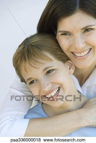 Stock Photo - Mother wilth arm around her daughter's shoulders, both looking away and smiling, portrait, close-up. Fotosearch