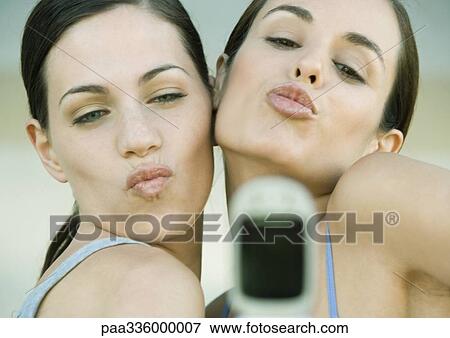 Stock Photo - Two young women posing and puckering toward cell phone. Fotosearch