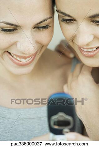 Two young women side by side looking down at a cell phone, both smiling, extreme close-up View Large Photo Image Stock Photo - Two young women side by side looking down at a cell phone, both smiling, extreme close-up. Fotosearch