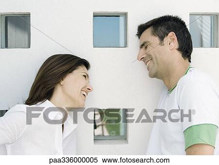 Stock Photography - Woman and husband, both leaning against wall with squared windows and smilling. Fotosearch