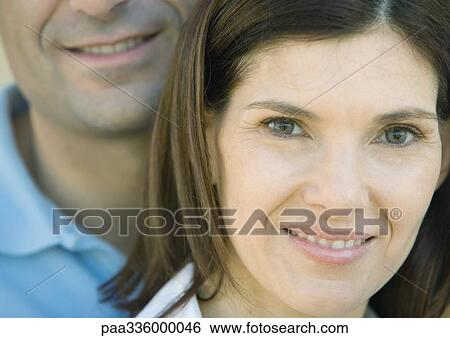 Woman smiling and looking at camera with her husband behind her, portrait, extreme close-up View Large Photo Image Stock Photograph - Woman smiling and looking at camera with her husband behind her, portrait, extreme close-up. Fotosearch