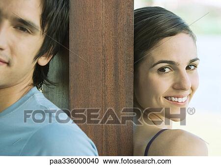Young couple standing back to back with a wooden post between them, smiling, portrait, partial view View Large Photo Image Stock Image - Young couple standing back to back with a wooden post between them, smiling, portrait, partial view. Fotosearch