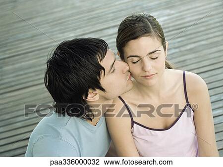 Stock Image - Young man kissing his girlfriend on the cheek, closed eyes, portrait. Fotosearch