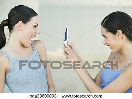 Young woman photographing a friend with cell phone, both laughing View Large Photo Image Stock Image - Young woman photographing a friend with cell phone, both laughing. Fotosearch