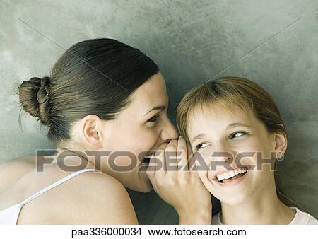 Young woman whispering to girl, both laughing, portrait, close-up View Large Photo Image Picture - Young woman whispering to girl, both laughing, portrait, close-up. Fotosearch