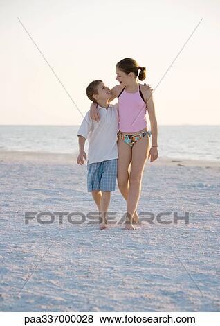 Stock Photo - Girl and boy walking with arms around each other's shoulder's on beach. Fotosearch
