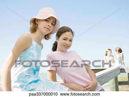 Stock Image - Preteen sisters leaning against wooden railing. Fotosearch