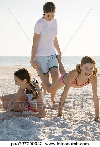 Three girls on the beach, one holding the other's legs like wheelbarrow View Large Photo Image Stock Image - Three girls on the beach, one holding the other's legs like wheelbarrow. Fotosearch