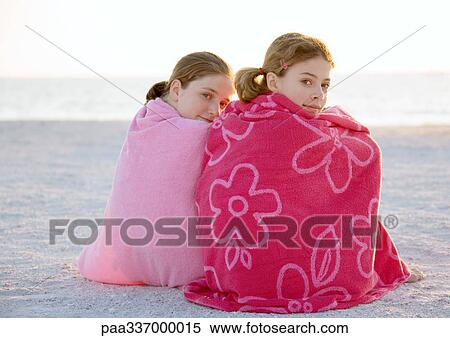 Stock Photography - Two girls sitting wrapped in towels on beach. Fotosearch