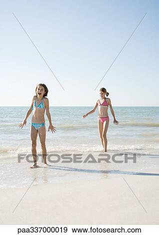 Stock Photo - Two girls walking on beach, one with mouth open in surprise. Fotosearch