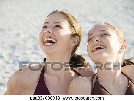 Stock Image - Two preteen girls laughing and looking up on beach. Fotosearch