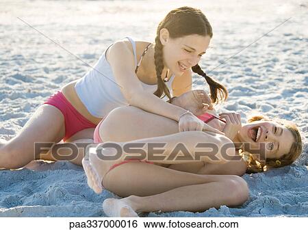 Stock Photograph - Two preteen girls on beach, one tickling the other. Fotosearch