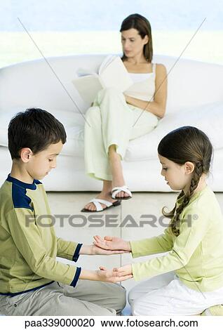Boy and girl playing game while mother reads in background View Large Photo Image Stock Image - Boy and girl playing game while mother reads in background. Fotosearch