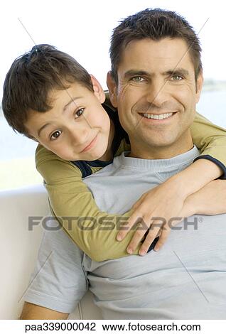 Stock Image - Boy hugging father from behind, portrait. Fotosearch
