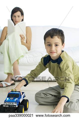 Boy playing with toy car while mother reads in background View Large Photo Image Stock Image - Boy playing with toy car while mother reads in background. Fotosearch