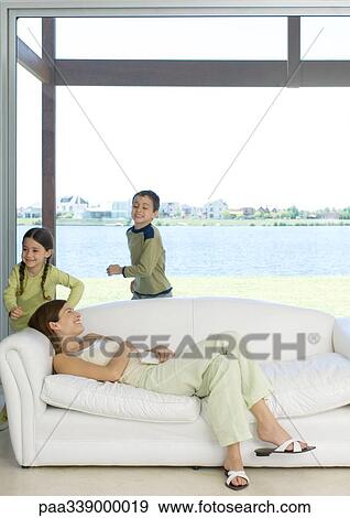Mother reclining on sofa while children run around her View Large Photo Image Stock Photo - Mother reclining on sofa while children run around her. Fotosearch