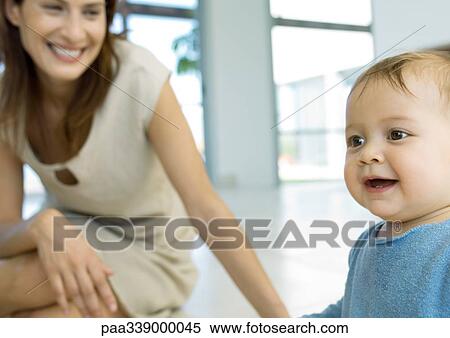 Stock Photography - Woman smiling and watching baby. Fotosearch