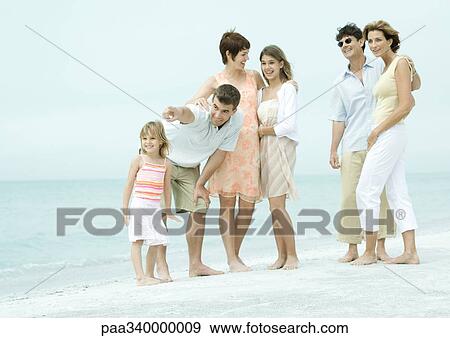 Stock Photo - Group standing on beach, man pointing. Fotosearch