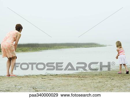 Woman and daughter leaning toward edge of water, rear view View Large Photo Image Stock Photo - Woman and daughter leaning toward edge of water, rear view. Fotosearch