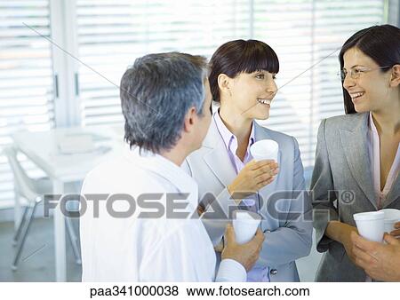 Business colleagues standing in office with cups in hands, chatting View Large Photo Image Stock Photo - Business colleagues standing in office with cups in hands, chatting. Fotosearch
